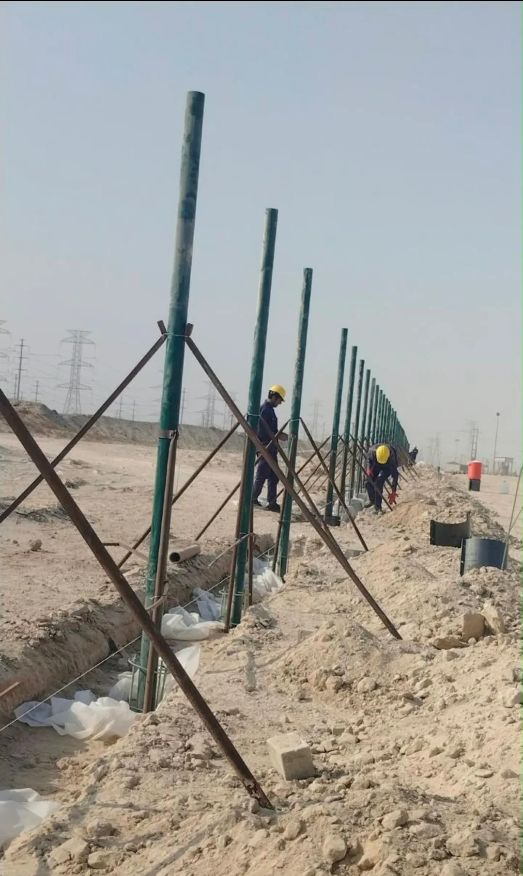 عمال يثبتون أعمدة السياج الأمني ويجهزون قواعده الخرسانية