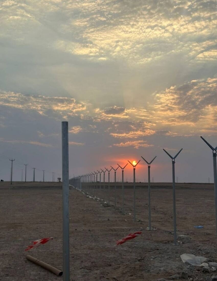 سياج شبكي مجلفن ممتد حول أرض وقت الغروب