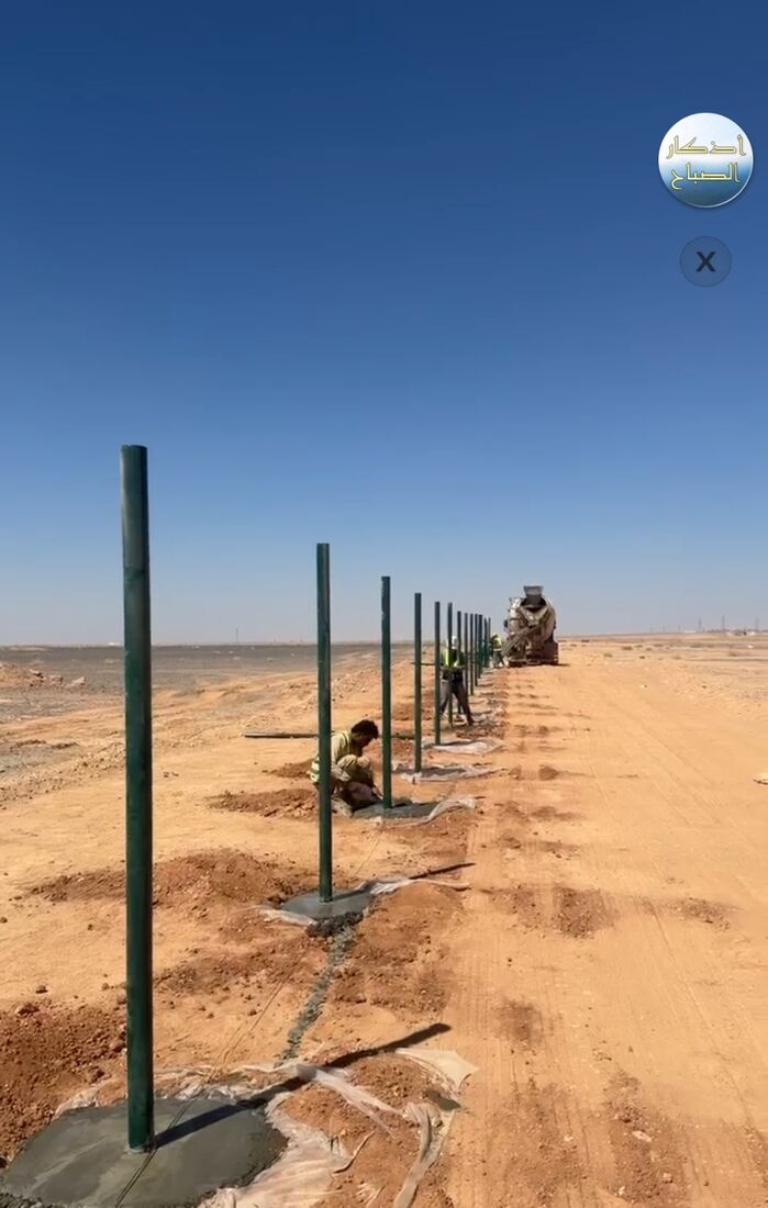فني يعمل على تركيب أعمدة شبك لمزرعة